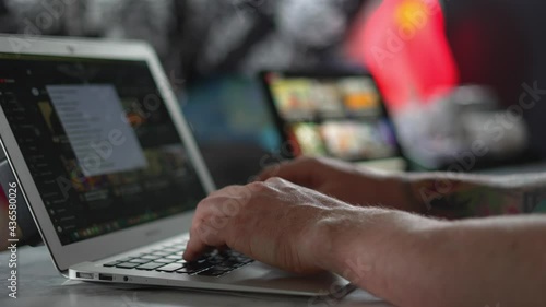 A person typing on a silver MacBook Air laptop computer on YouTube, at a white desk with iPad screen in back ground, working from home after Covid 19 pandemic lockdown restrictions. In 4k 60fps.