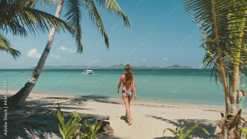 Sensual girl in bikini walking on beach. Turquoise ocean water with sailboat. Sexy woman with perfect slim body in stylish swimwear on paradise tropic resort. Summer vacation at Bali, Indonesia, Asia Sensual girl in bikini walking on beach. Turquoise ocean water with sailboat. Sexy woman with perfect slim body in stylish swimwear on paradise tropic resort. Summer vacation at Bali, Indonesia, Asia