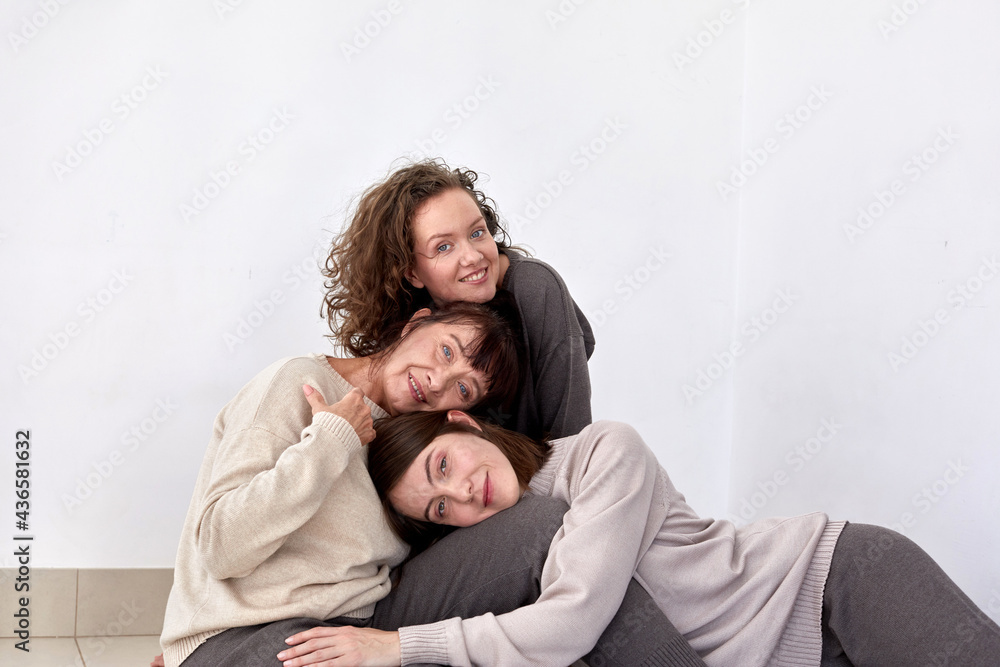 Content mature mother hugging adult daughters on white background in studio and looking at camera Content mature mother hugging adult daughters on white background in studio and looking at camera