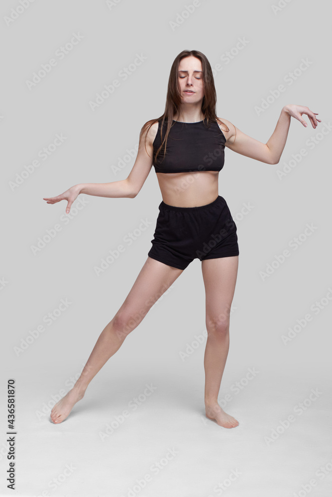 Young slim athletic girl, with long hair, in a black top and shorts, dancing in the white studio Young slim athletic girl, with long hair, in a black top and shorts, dancing in the white studio