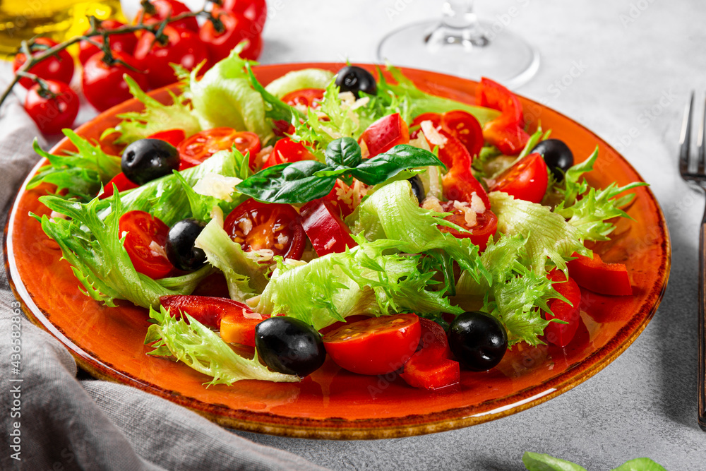  Simple summer salad of lettuce, tomatoes with olives and olive oil on a red plate close-up