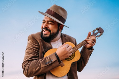 Outdoor of a young Latin American man playing cavaquinho or ukulele. Brazilian musician. photo