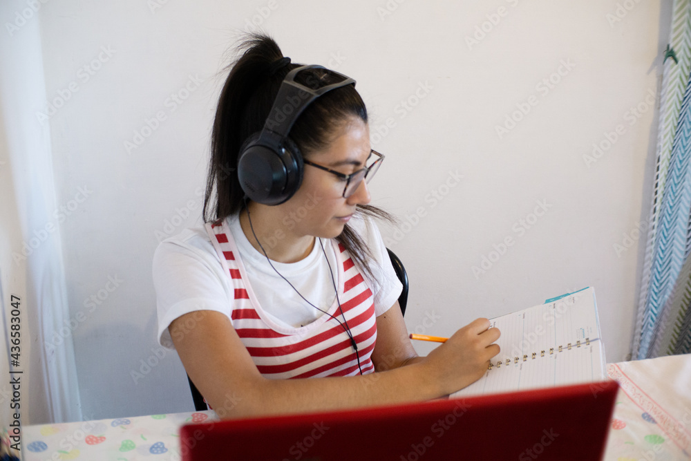 Woman wearing headphones, using laptop, writing notes and smiling, concept of online classes Woman wearing headphones, using laptop, writing notes and smiling, concept of online classes