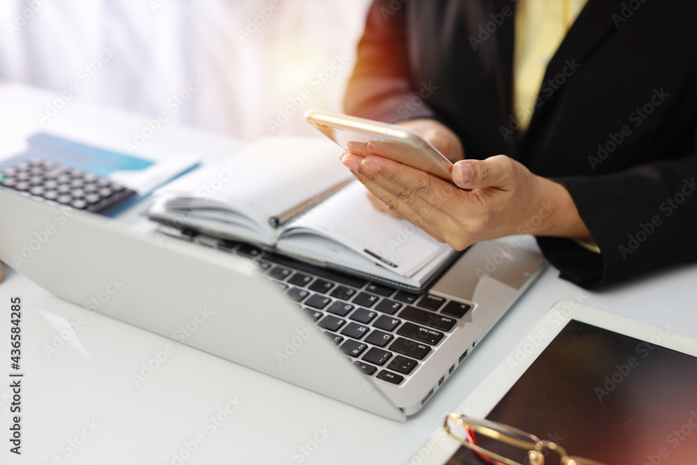 Woman hands in black suit sitting and holding mobile phone using laptop computer on table for online payment or shopping online. Business woman using smart phone while working. E-Banking concept Woman hands in black suit sitting and holding mobile phone using laptop computer on table for online payment or shopping online. Business woman using smart phone while working. E-Banking concept