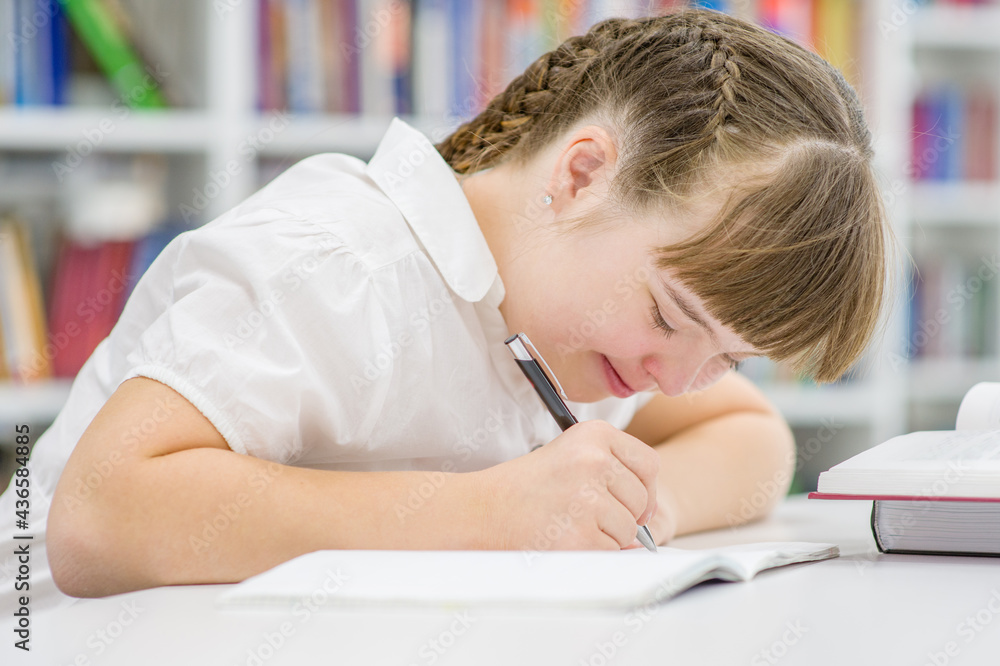 Smiling girl with down syndrome doing homework at library. Education for disabled children concept
