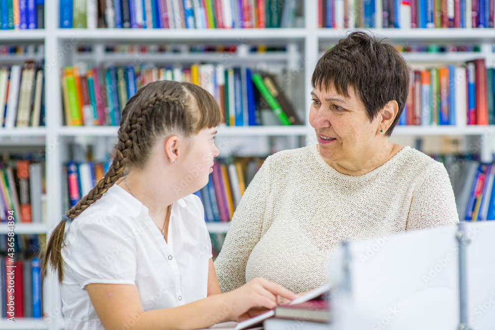 Teacher and girl with syndrome down read a book at library. Education for disabled children concept Teacher and girl with syndrome down read a book at library. Education for disabled children concept