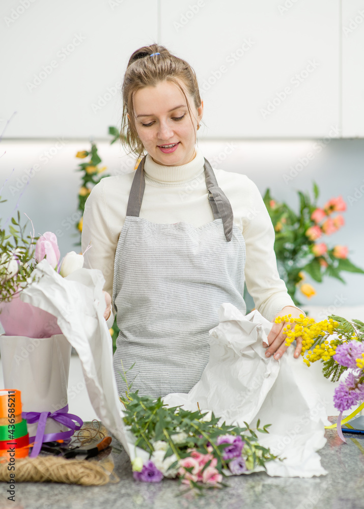 Florist wearing apron wrapping a bouquet of beautiful colorful flowers inside her floral shop Florist wearing apron wrapping a bouquet of beautiful colorful flowers inside her floral shop