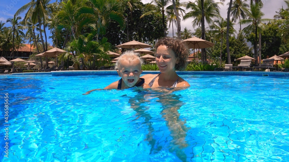 First attempts to swim. Young mother teaches her toddler baby girl to swim in a pool while on vacations