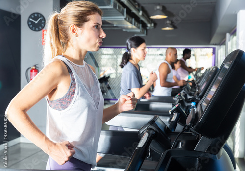Slender athletic positive european girls running on treadmill in fitness club