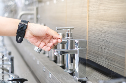 Male hand choosing stainless steel water tap in furniture store. Home improvement for domestic kitchen.