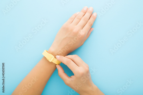 Yellow mosquito repellent band on young adult woman wrist on light blue table background. Pastel color. Closeup. Point of view shot. Protection from insects. Top down view.