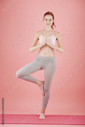 Cheerful young fit woman standing on yoga mat in tree pose that improves balance and concentration