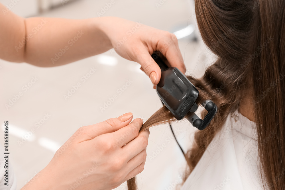 Fototapeta premium Female hairdresser curling hair of client in beauty salon, closeup