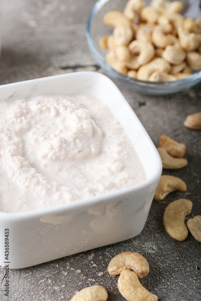 Bowl with cashew sour cream and nuts on grey background, closeup