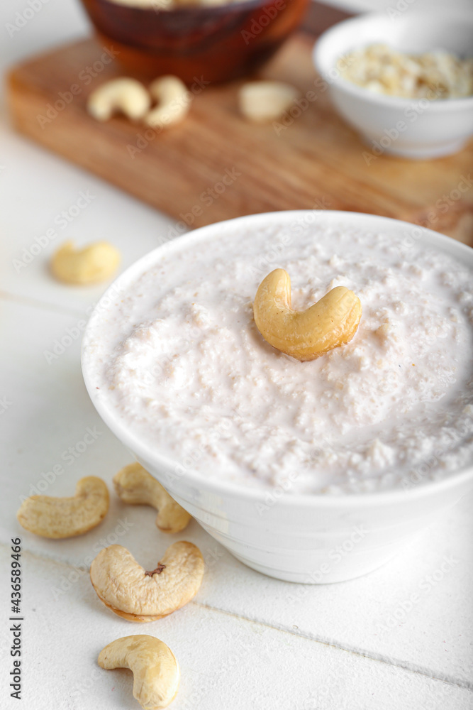 Bowl with cashew sour cream and nuts on light wooden background, closeup