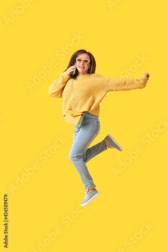 Jumping young woman talking by mobile phone on color background