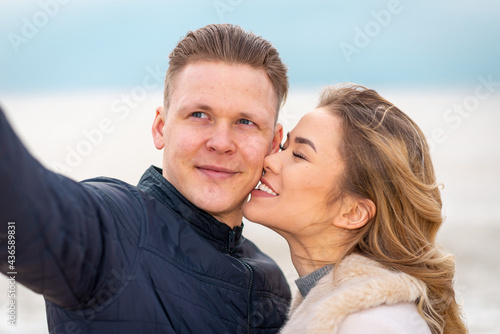 Beautiful young happy woman hugging cuddle young boyfriend while taking selfie photo on sunny beach.Close up. © ARVD73