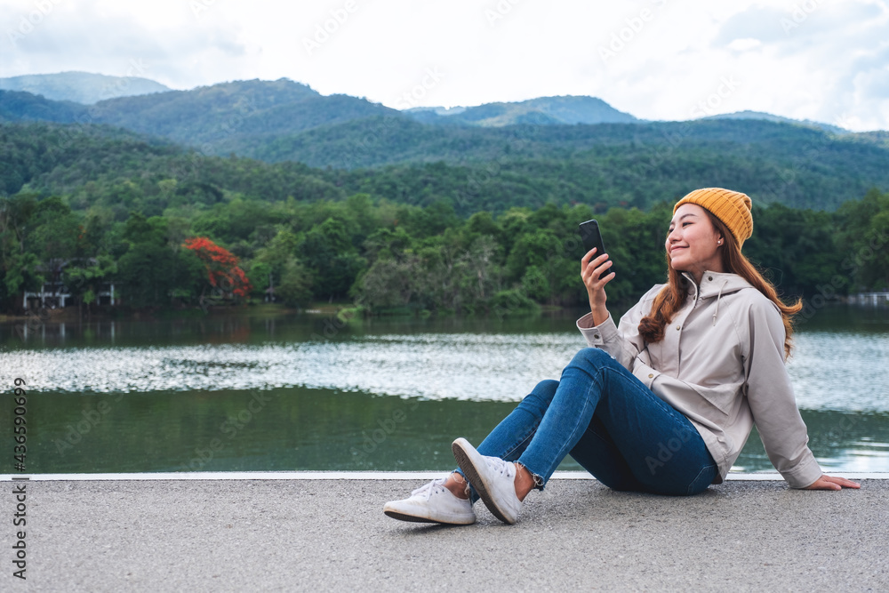 Fototapeta premium A young asian woman holding and using mobile phone while traveling mountains and lake