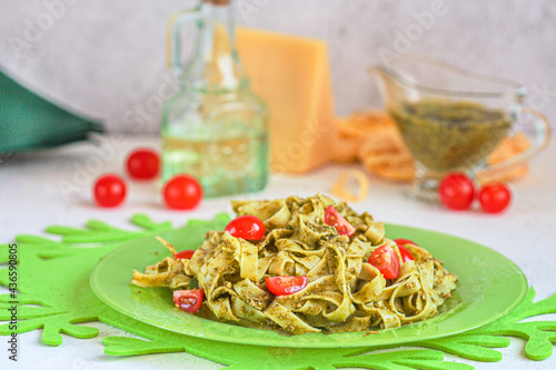 Fettuccine pasta with pesto, pine nuts, cherry tomatoes and grated Parmesan on a green plate. Italian cuisine. Home cooking.