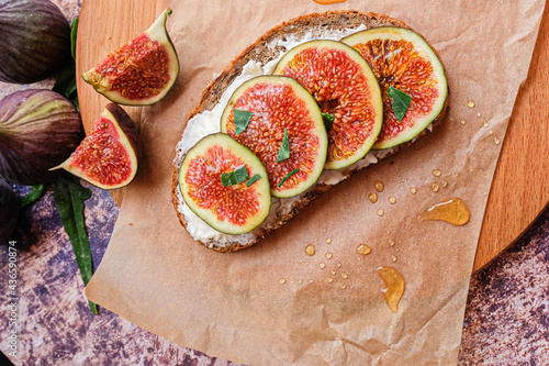 Figs. Sandwiches with figs, cheese, arugula, honey and nuts on wooden board over textured purple backdrop. Next to pieces of fresh figs with cinnamon. Homemade. Everyday autumn kitchen.