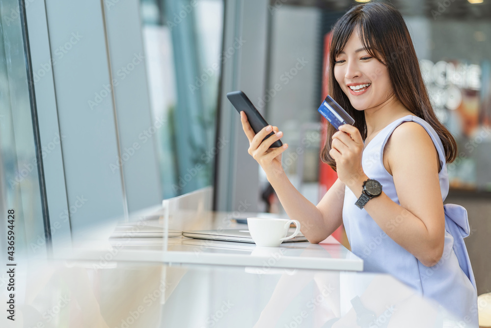 Asian woman using credit card with mobile phone for online shopping in modern coffee shop, technology money wallet and online payment concept, credit card mockup