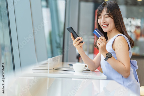 Obraz na płótnie Asian woman using credit card with mobile phone for online shopping in modern coffee shop, technology money wallet and online payment concept, credit card mockup w salonie