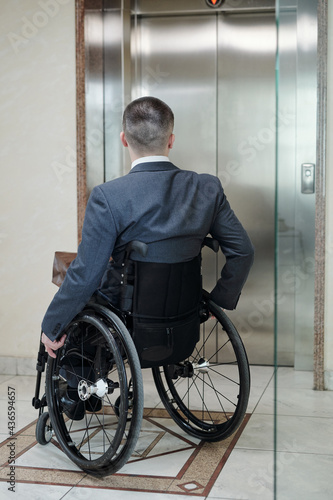 Disabled man in wheelchair waiting for elevator inside office building
