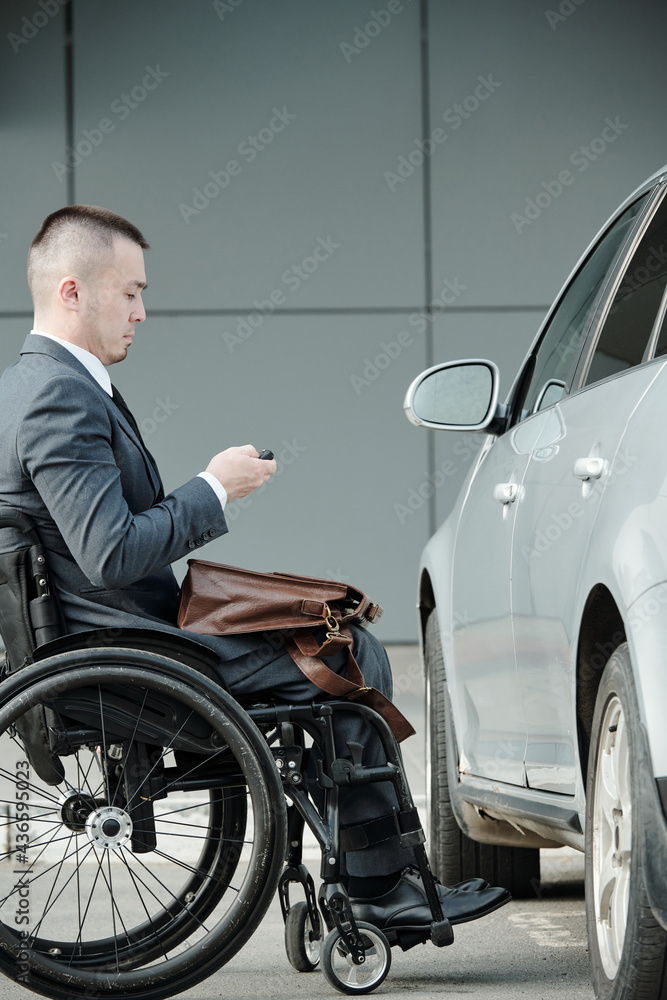 Businessman in wheelchair pressing button on car alarm remote control before going to office