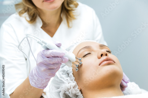 Facial skin care and protection. A young woman at a beauticians appointment looks in a mirror. A specialist examines the skin