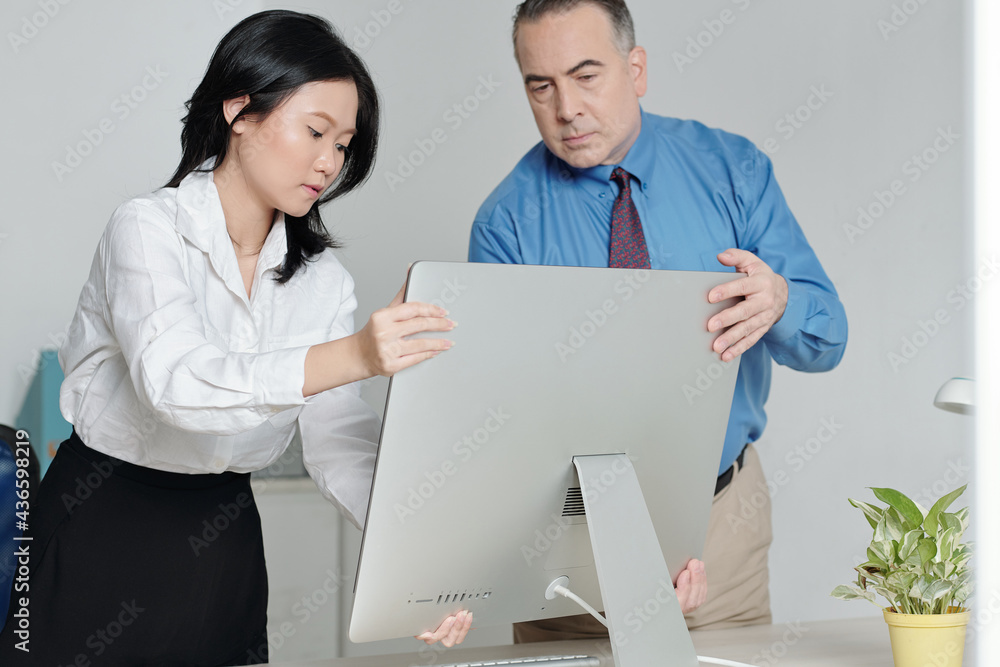 Mature serious man helping new colleague to put computer at her office desk Mature serious man helping new colleague to put computer at her office desk