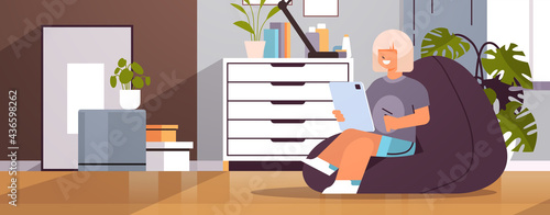schoolgirl using tablet pc happy girl sitting on beanbag and doing homework education concept living room interior