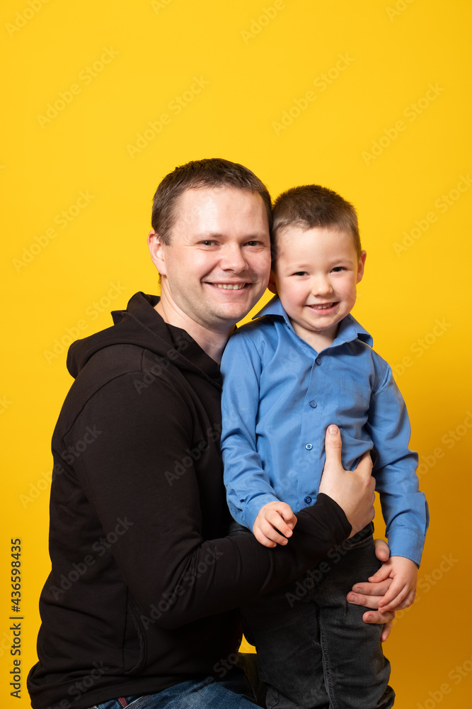 Cheerful happy father with baby boy playing. Young dad with his son laugh and smile on a yellow background. 