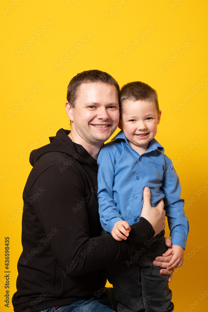 Cheerful happy father with baby boy playing. Young dad with his son laugh and smile on a yellow background. Cheerful happy father with baby boy playing. Young dad with his son laugh and smile on a yellow background.