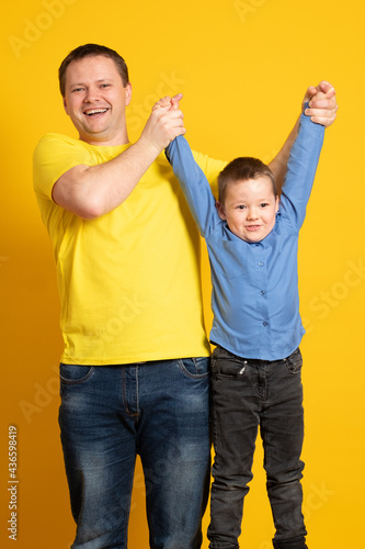 Happy father's day! Cute father and son hugging on yellow background. Portrait of a dad with a baby boy smiling and hugging. Family concept.