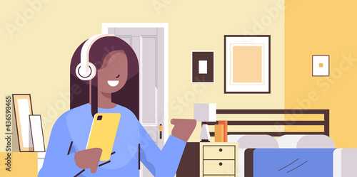 african american schoolgirl using smartphone and listening to music in headphones