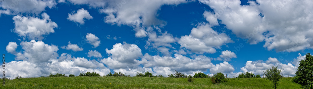 Ein mit Schönwetterwolken übersähter Himmel mit einer hügeligen Wiese im Vordergrund Ein mit Schönwetterwolken übersähter Himmel mit einer hügeligen Wiese im Vordergrund