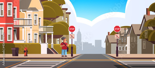 schoolboy with backpack standing near red stop road sign on city street road safety concept full length horizontal