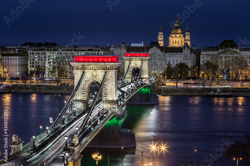 Budapest  Hungary - The world famous illuminated Szechenyi Chain Bridge  Lanchid  by night  lit up with national red  white and green colors with St.Stephen s Basilica at background on revolution day