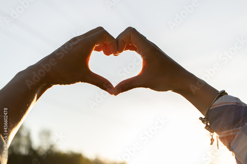 Women's hands in the shape of a love heart on the background of a beautiful summer sunset. Silhouette of female hands at sunset. Symbol of love and freedom