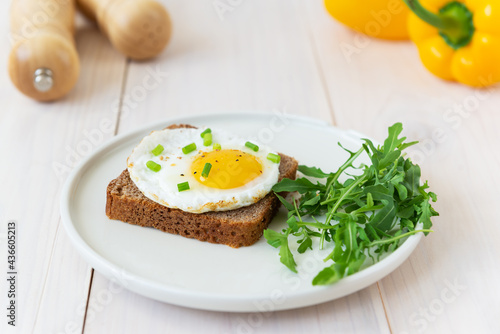 Toast with fried eggs with green onions, arugula and spices in a plate on a wooden table.