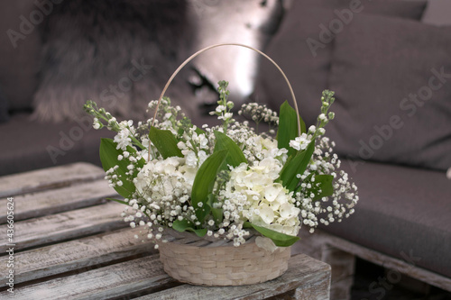 Beautiful flowers in a basket on white wooden table.