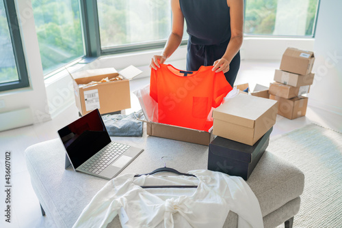 Selling new or used clothes online with internet app on laptop computer screen. Woman packing fashion clothing in mailing box for shipping orders from home. Small business. photo