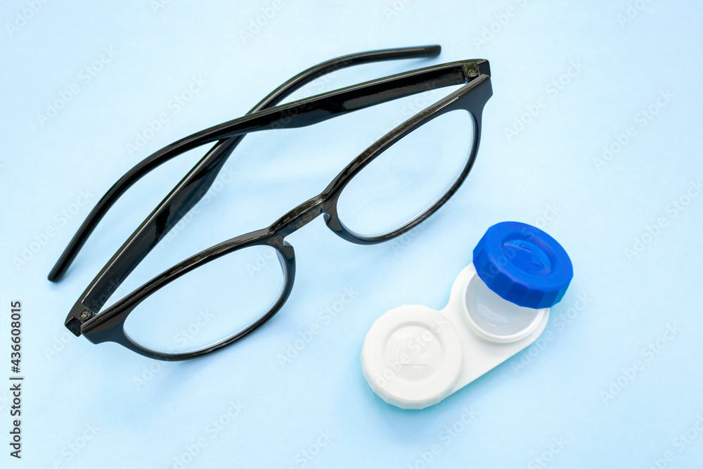 Container with contact lenses and glasses with black frames, vision correction concept,ophthalmology, eye health care, eyesight test, eyewear optics store on light blue medical background Container with contact lenses and glasses with black frames, vision correction concept,ophthalmology, eye health care, eyesight test, eyewear optics store on light blue medical background