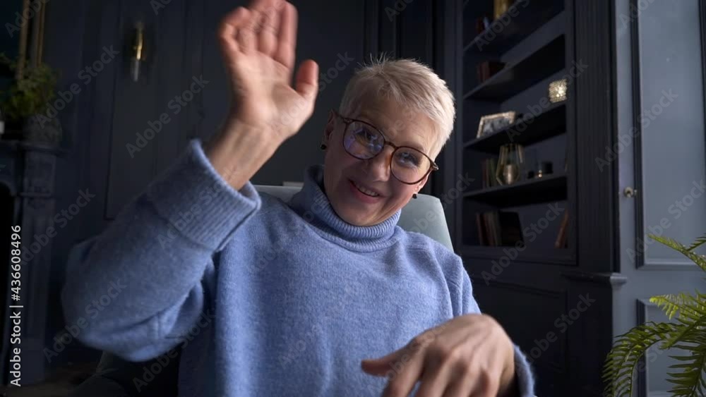 Woman waving hand in front of screen and talking while sitting in armchair at home interior akspb. Woman waving hand in front of screen and talking while sitting in armchair at home interior akspb.
