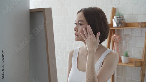 attractive beautiful short hair asian woman worry looking into mirror for face skin care condition. Frustrated Young female Examining Her Face While Looking At The Mirror in bathroom. annoy facial age
