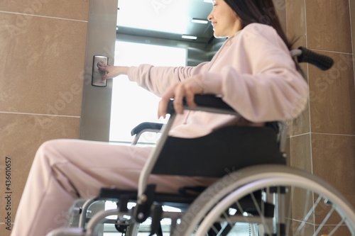 Smiling woman in wheelchair presses button of elevator