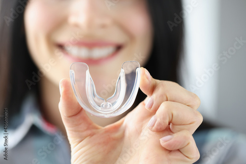 Smiling woman holds transparent plastic mouth guard in her hand photo