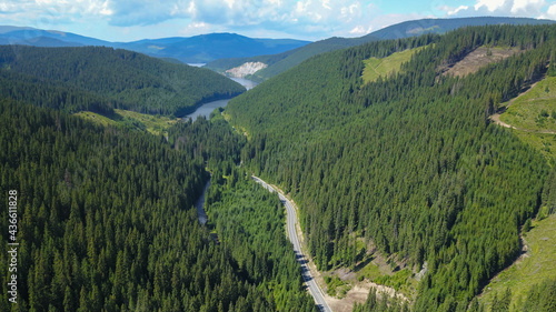 Aerial drone view above Oasa Lake and Sureanu Massif with its high altitude peaks and wild spruce forests. Below, Transalpina road winds through the valley. Spring time, Carpathia, Romania.