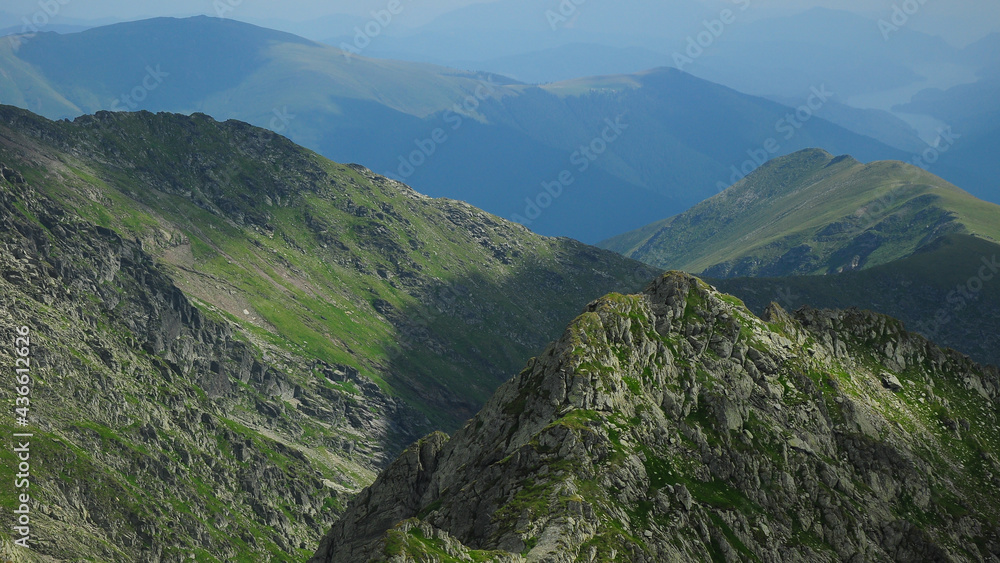 Hiking on the steep mountain peaks of Fagaras Mountains, Romania. In the far right Vidraru Lake can be seen in the valley. Carpathia, Romania.