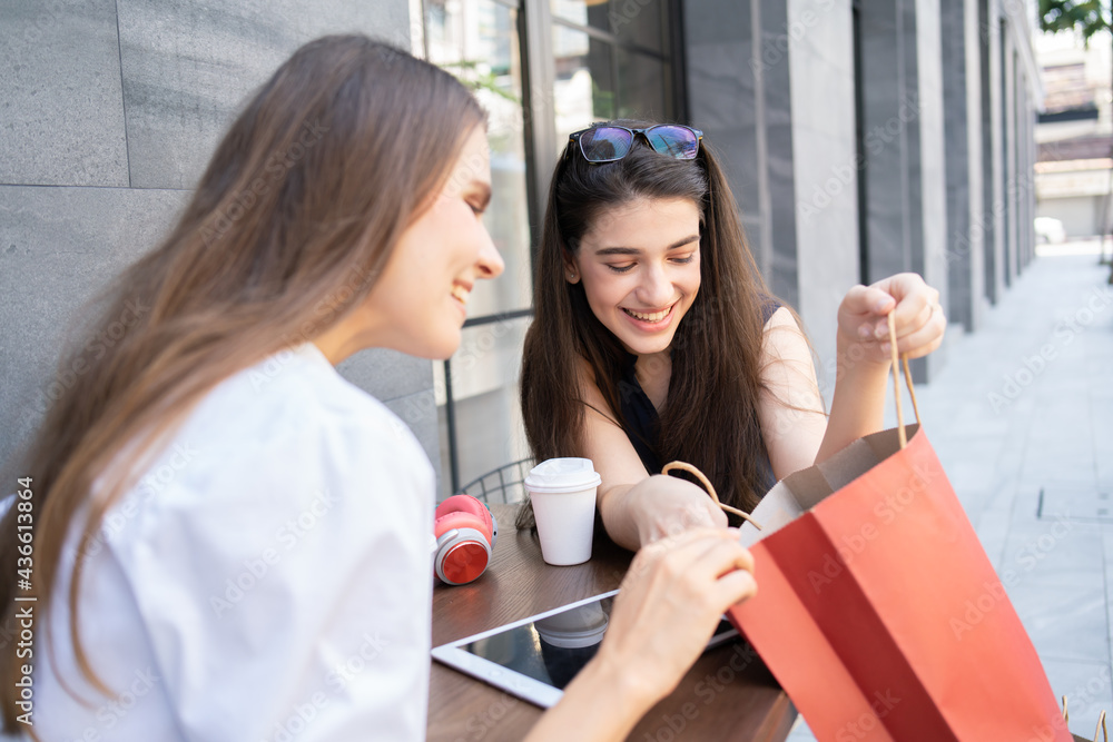 two woman having coffee break and looking something in the shopping bags two woman having coffee break and looking something in the shopping bags